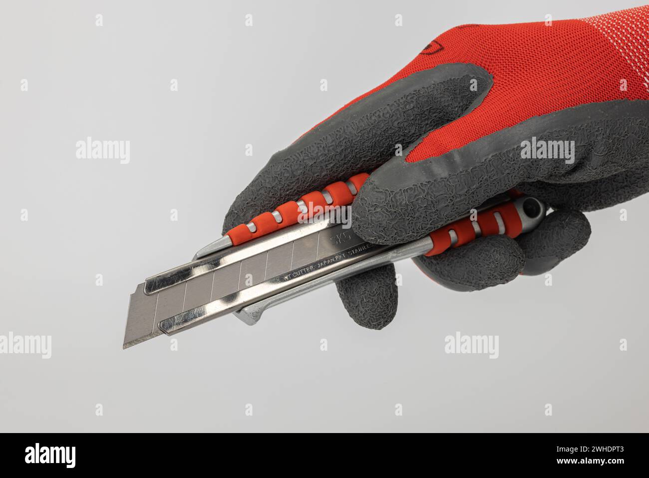 Man's hand with work glove holding cutter knife with 18 mm snap-off blade, die-cast aluminum with rubberized red grip zone, white background, Stock Photo