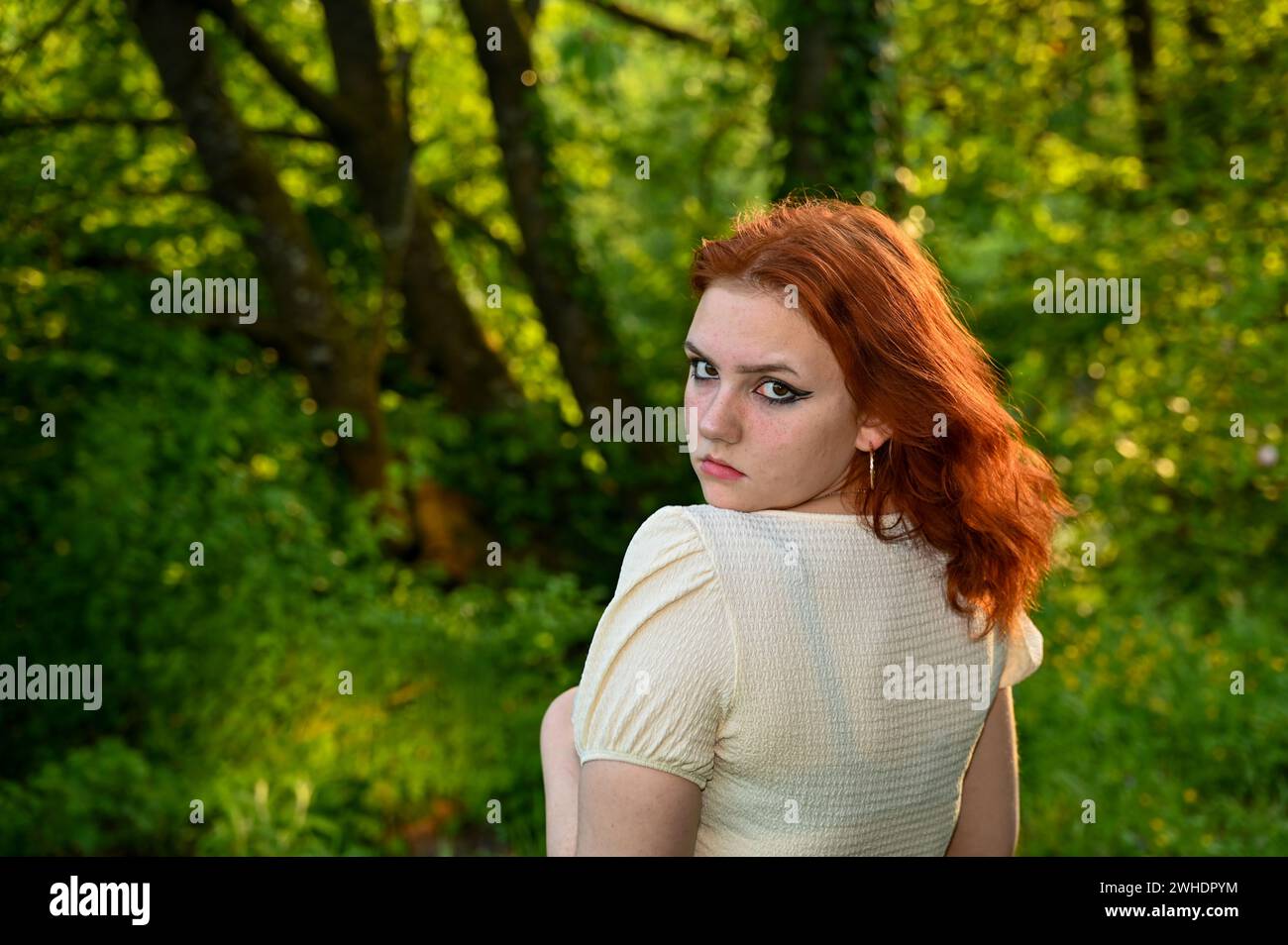 Portrait of a young redhead girl in green nature, looking seriously at ...