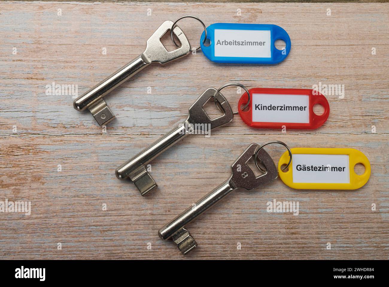 Three colored bearded keys with key hanger, labeled ëstudyë, childrenës roomë, ëö€°stezimmerë, wooden background, Stock Photo