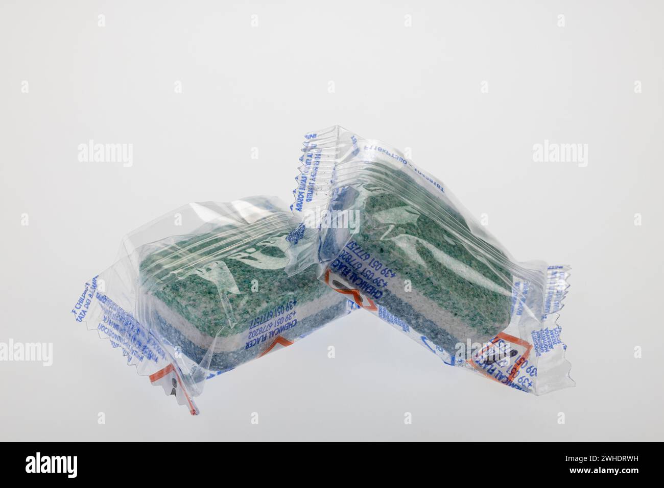 Two dishwashing detergent tabs in foil packaging with hazard pictogram, hazard warning, caution