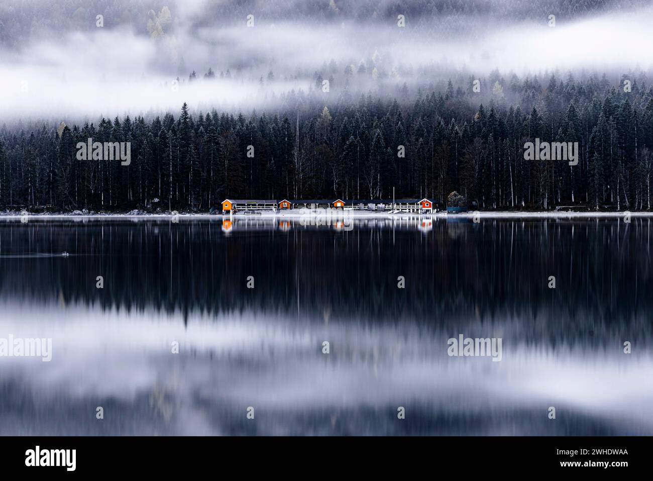 Eibsee with view of southern shore with boathouses and coniferous forest in the fog, Wettersteingebirge, Zugspitze, Garmisch-Partenkirchen, Bavaria, Germany Stock Photo
