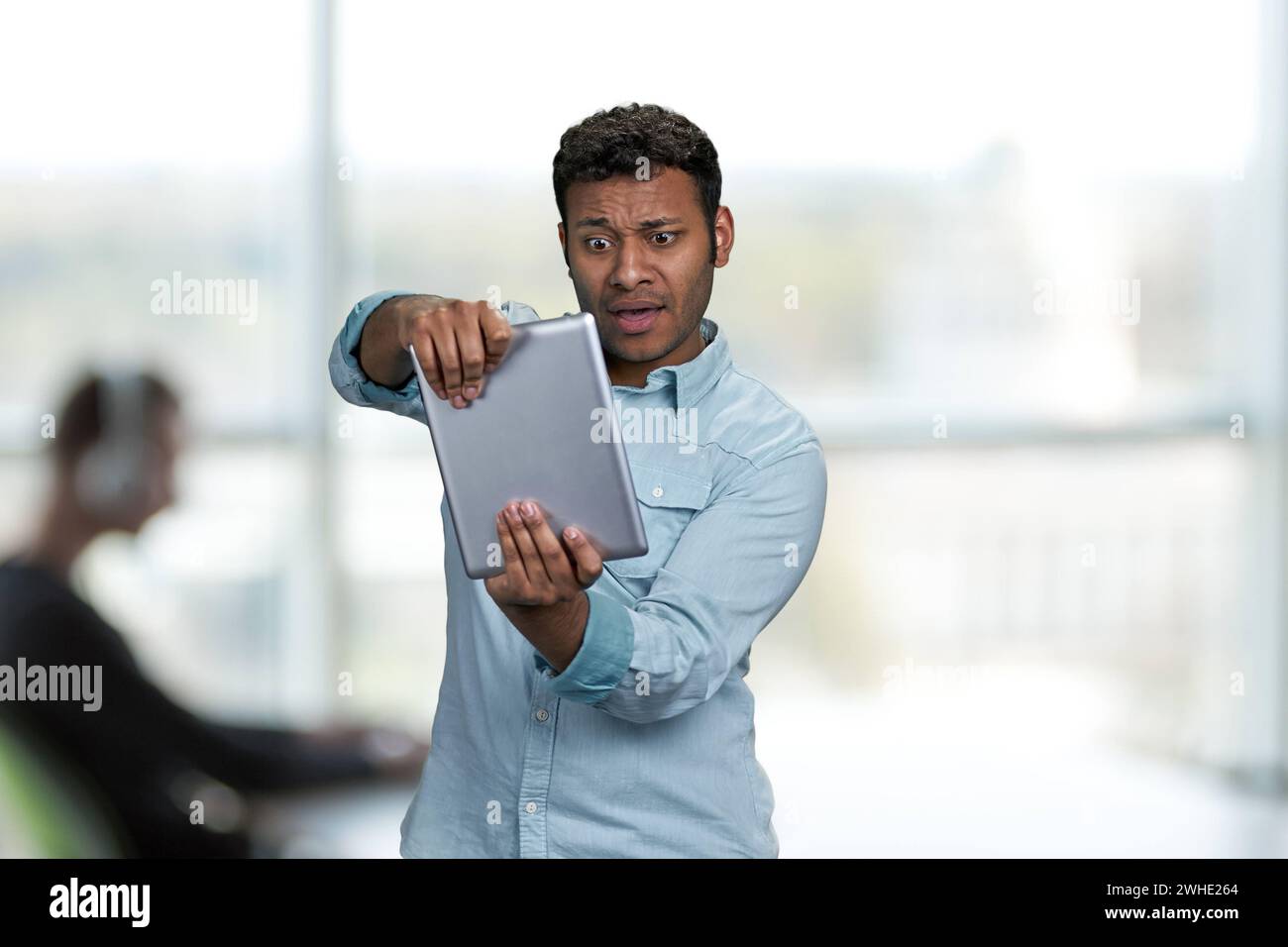 Ecstatic young man playing game on digital tablet. Office interior blur ...