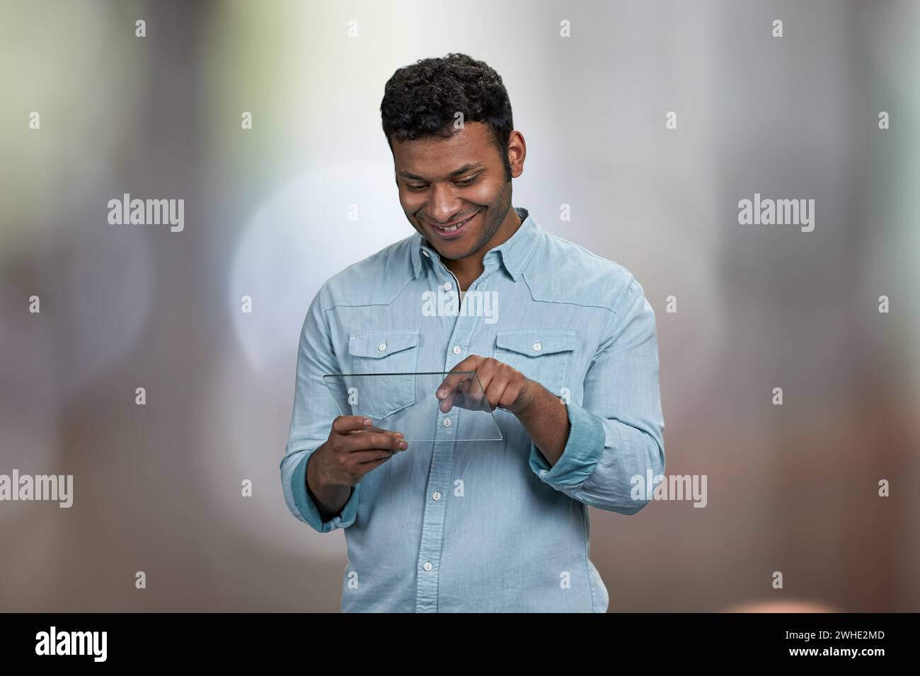 Smiling young man using transparent digital tablet. Abstract bokeh background. Stock Photo