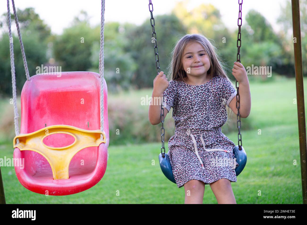 hermosa niña rubia de 8 años disfruta de la naturaleza en un escenario al aire libre lleno de verdor y luz mientras se columpia con gracia Stock Photo