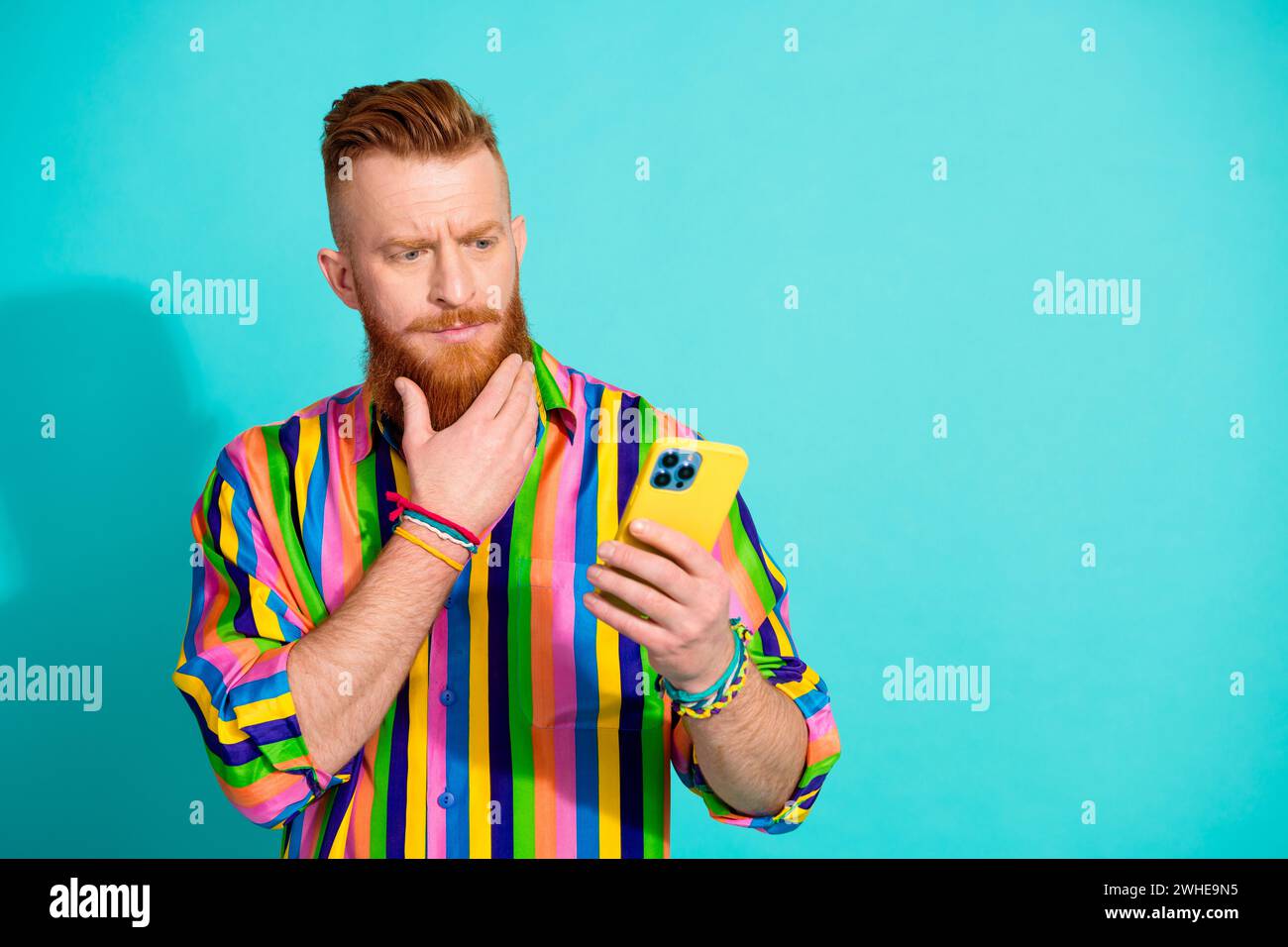 Photo of thoughtful irish man in striped shirt touching his beard when choosing taxi economy or vip class isolated on blue color background Stock Photo