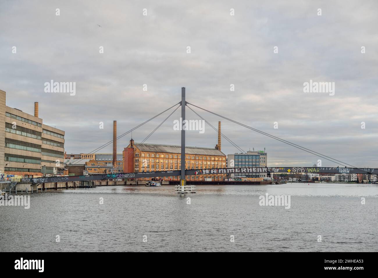 The former KWO (Kabelwerk Oberspree) listed building and the Kaisersteg Brucke in the foreground on a cloudy day, Treptow - Koepenick, Berlin, Germany Stock Photo