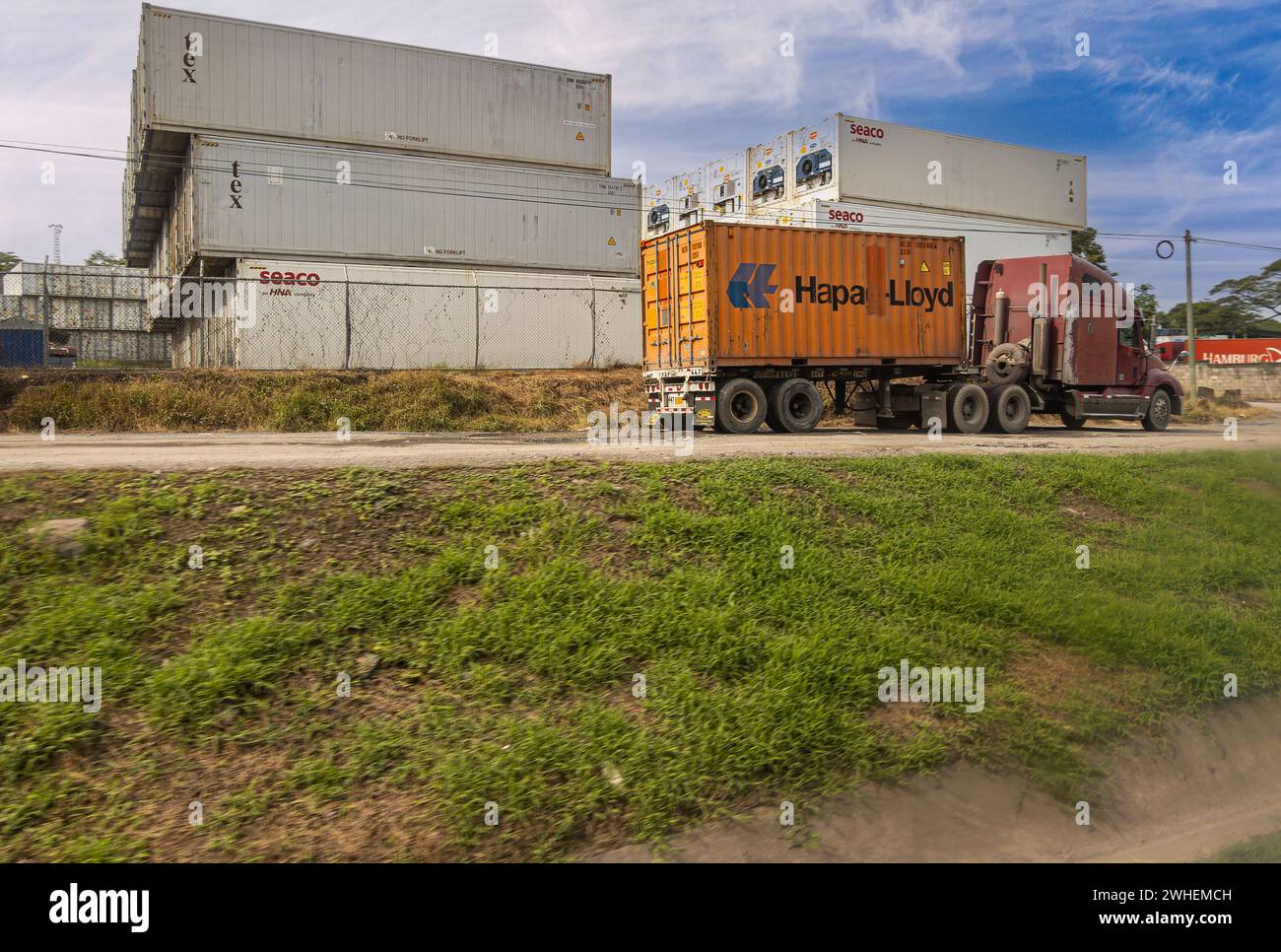 Costa Rica, San Juan Grande - July 22, 2023: Truck arrives at Shipping container storage field along Highway 27. Stacks of them. Blue cloudscape and g Stock Photo