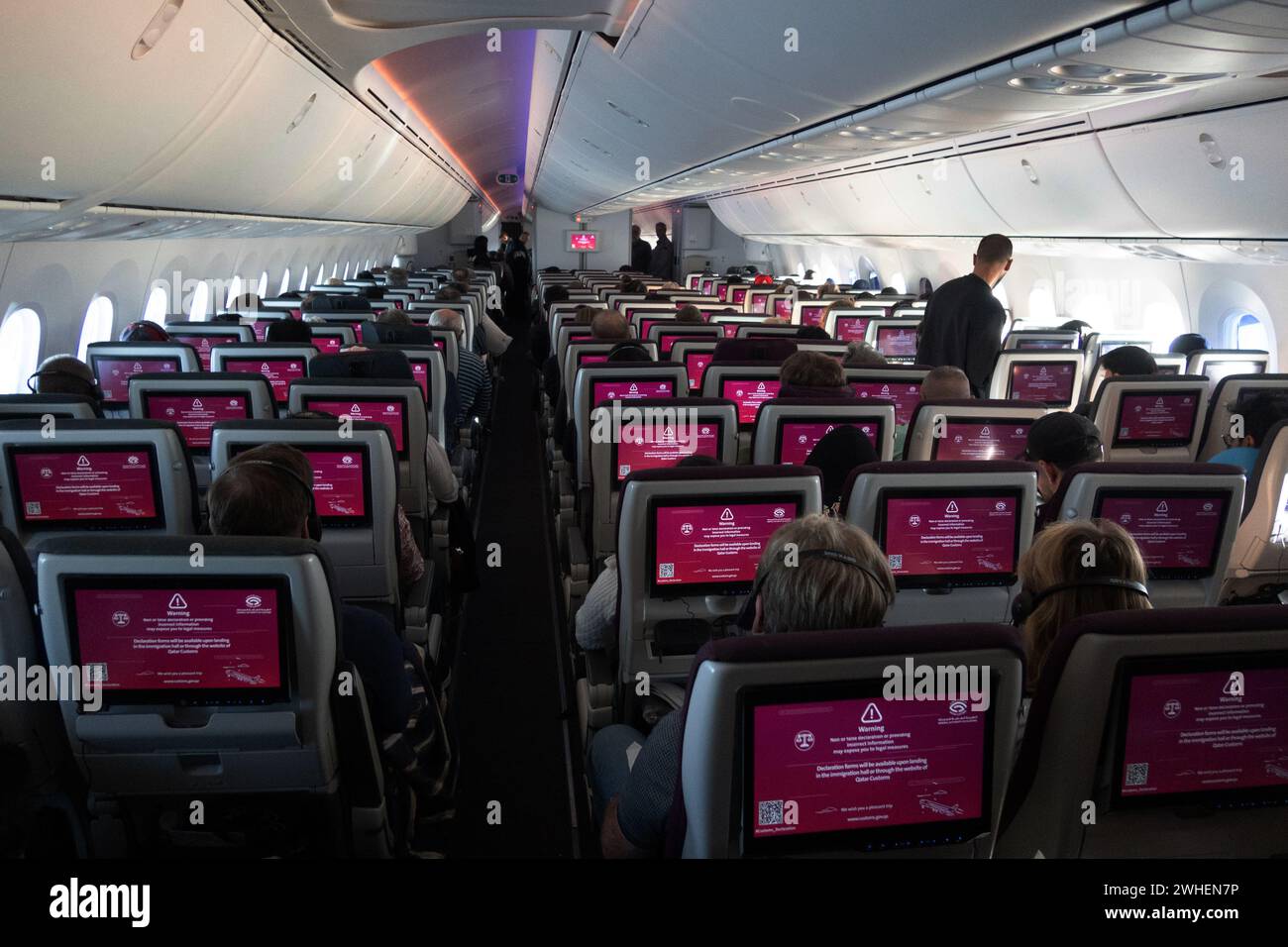"30.10.2023, Quatar, , Doha - Passengers in an airplane cabin receive information about customs regulations when entering the country via the on-board Stock Photo