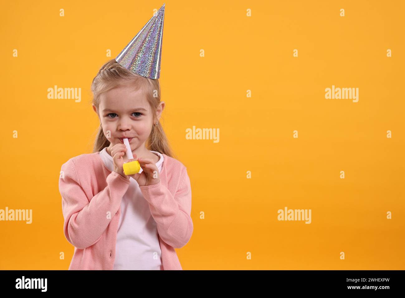 Birthday celebration. Cute little girl in party hat with blower on ...