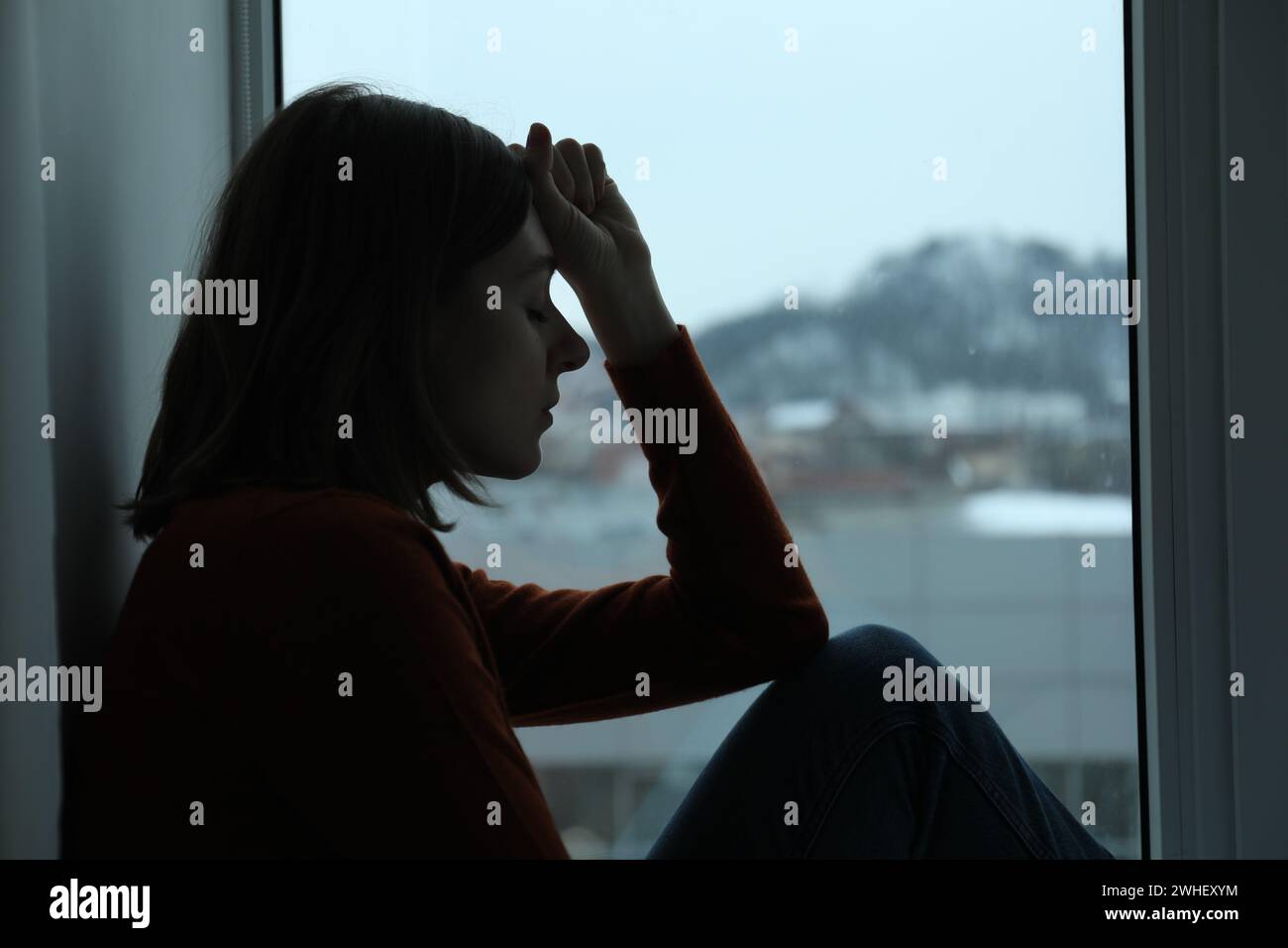 Sad young woman sitting on windowsill near window at home Stock Photo ...