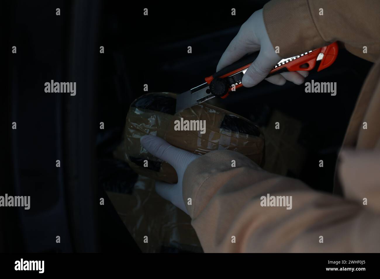 Man opening package of narcotics with stationery knife on dark background, closeup. Space for text Stock Photo