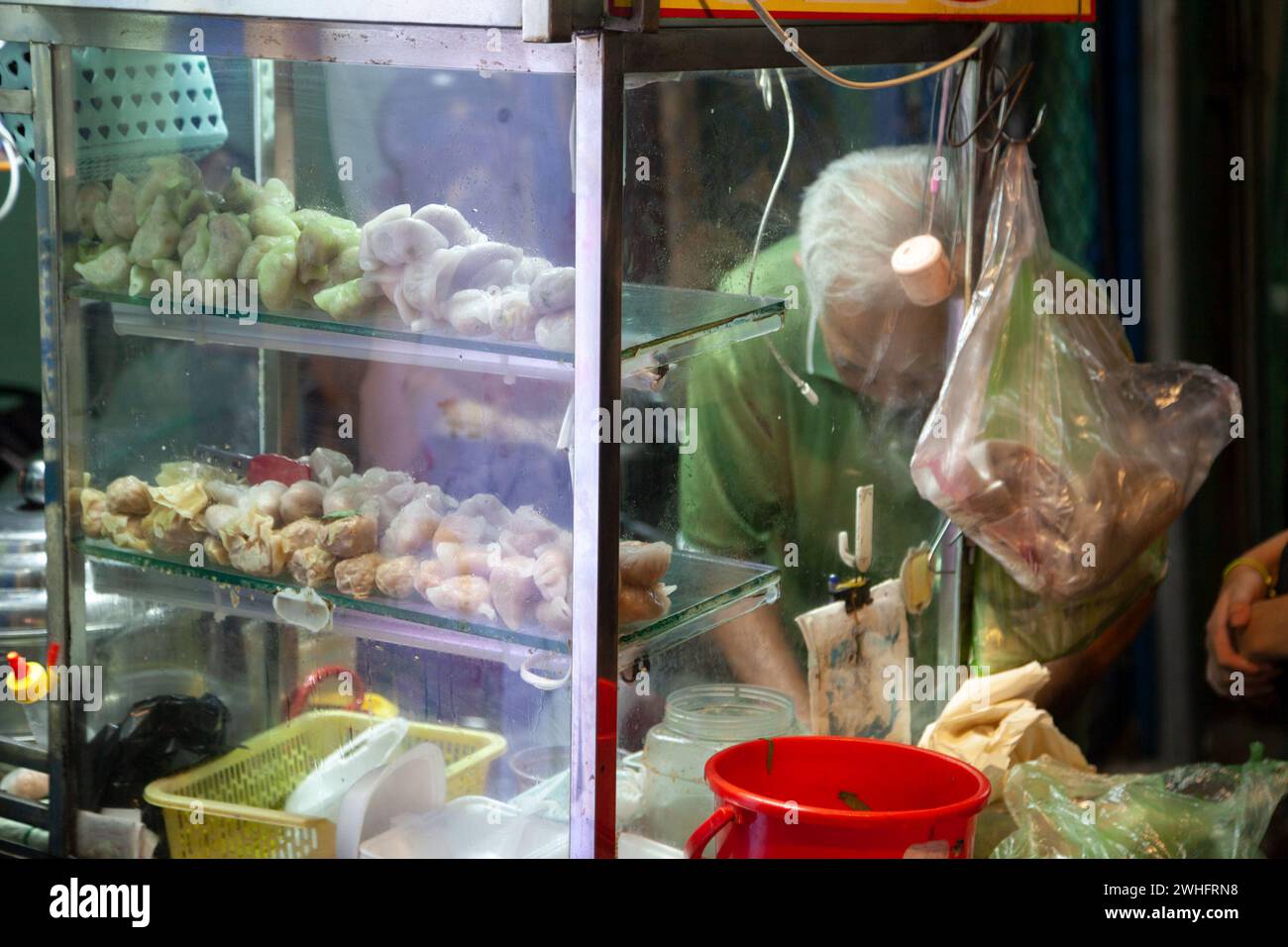 Ho Chi Minh City, Vietnam - February 2, 2024: An old Asian man behind the glass of a stall cooking a traditional Vietnamese dish in the evening. Dumpl - Stock Image