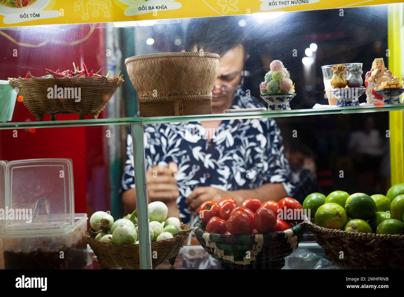 Ho Chi Minh City, Vietnam - February 2, 2024: A middle-aged Asian man behind the glass of a stall cooking a traditional Vietnamese dish in the evening - Stock Image