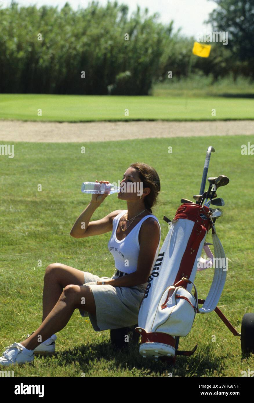 pretty dark hair young woman resting on green golf drinking water bottle south of france Stock Photo