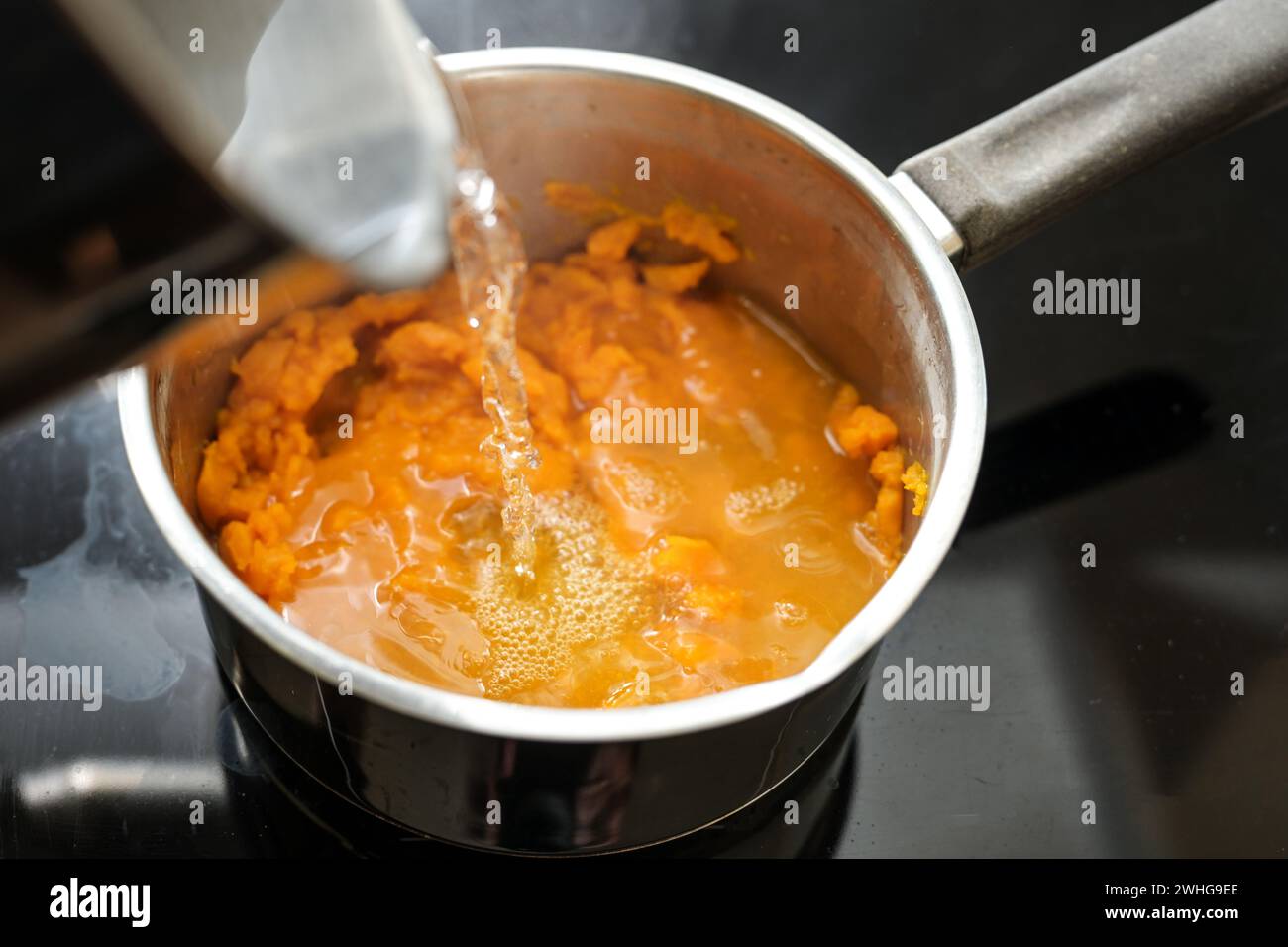 Pureed carrots are poured with boiling water in a steel pot, cooking a healthy digestible vegetable soup, invented by Professor Stock Photo