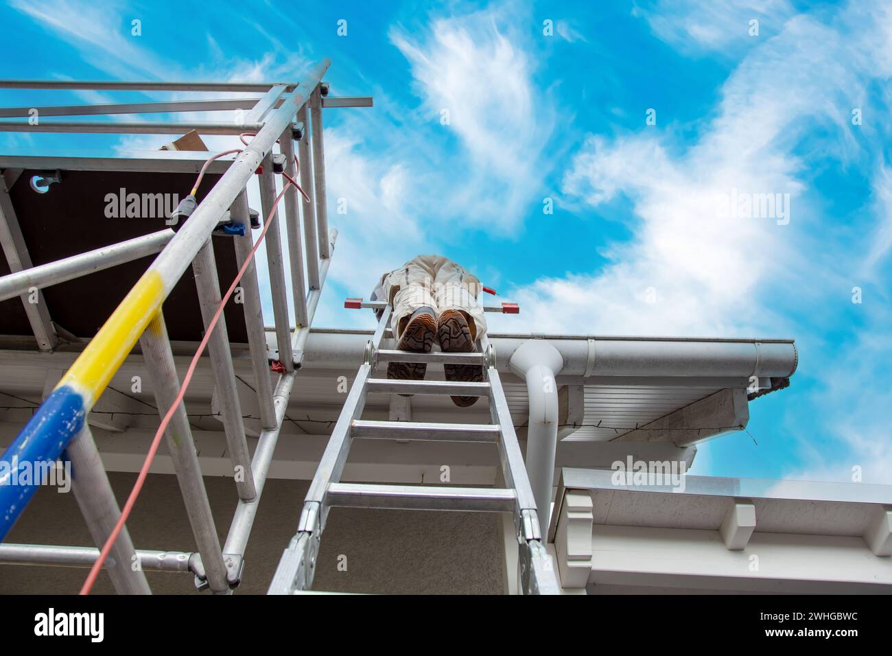 Roofer, worker on the rooftop, standing on a ladder. Roofing work. scaffolding on construction site Stock Photo