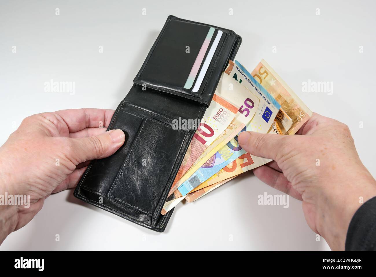 Hands taking various euro banknotes out of a black leather wallet, money and finance concept, light gray background Stock Photo