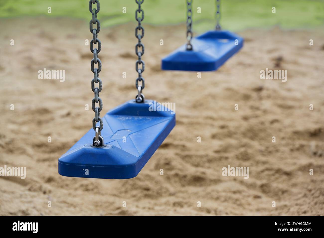 Two empty blue plastic swings for children hang from metal chains in a