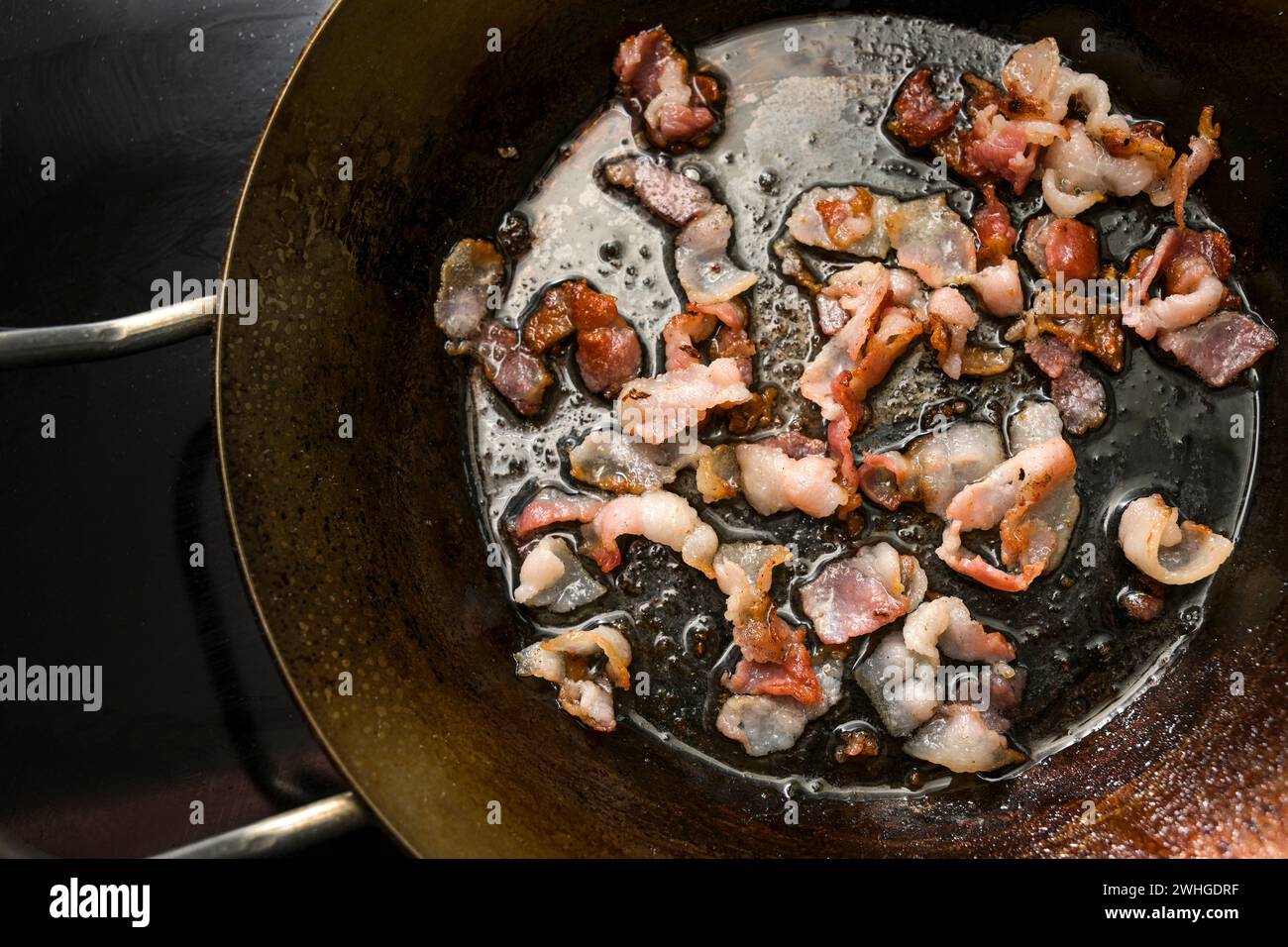 Chopped bacon crispy fried in an iron pan on the black stove, copy space, high angle view from directly above Stock Photo