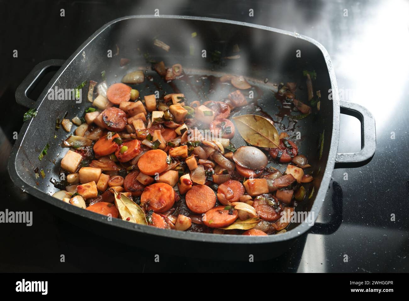 Roasted vegetables for a tasty sauce base in a black cooking pan with carrots, onions, leeks, celery and bay leaves, copy space, Stock Photo
