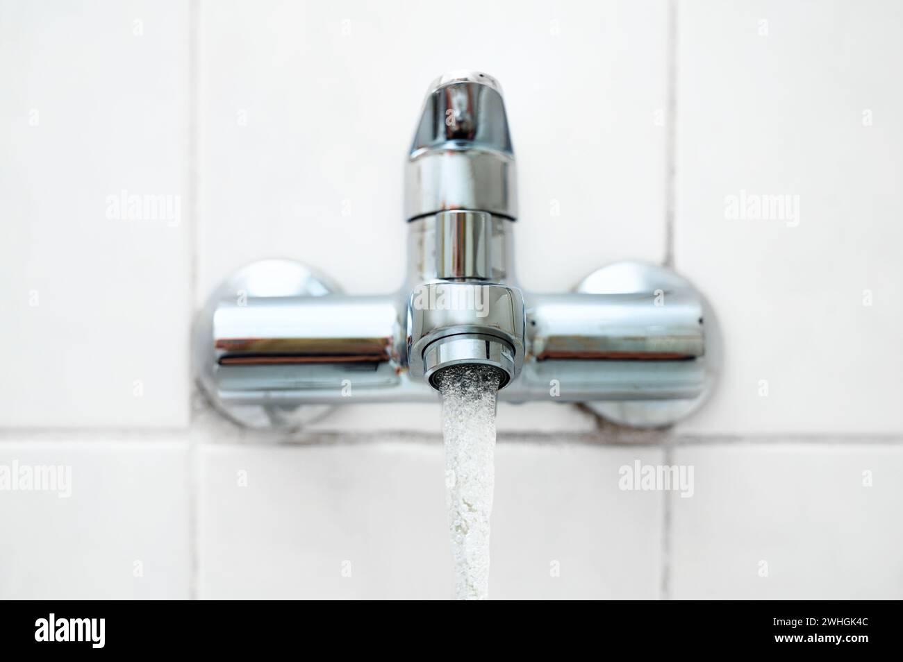 Bath fitting or tap with running water on a white tiled wall in an older bathroom, copy space, selected focus Stock Photo