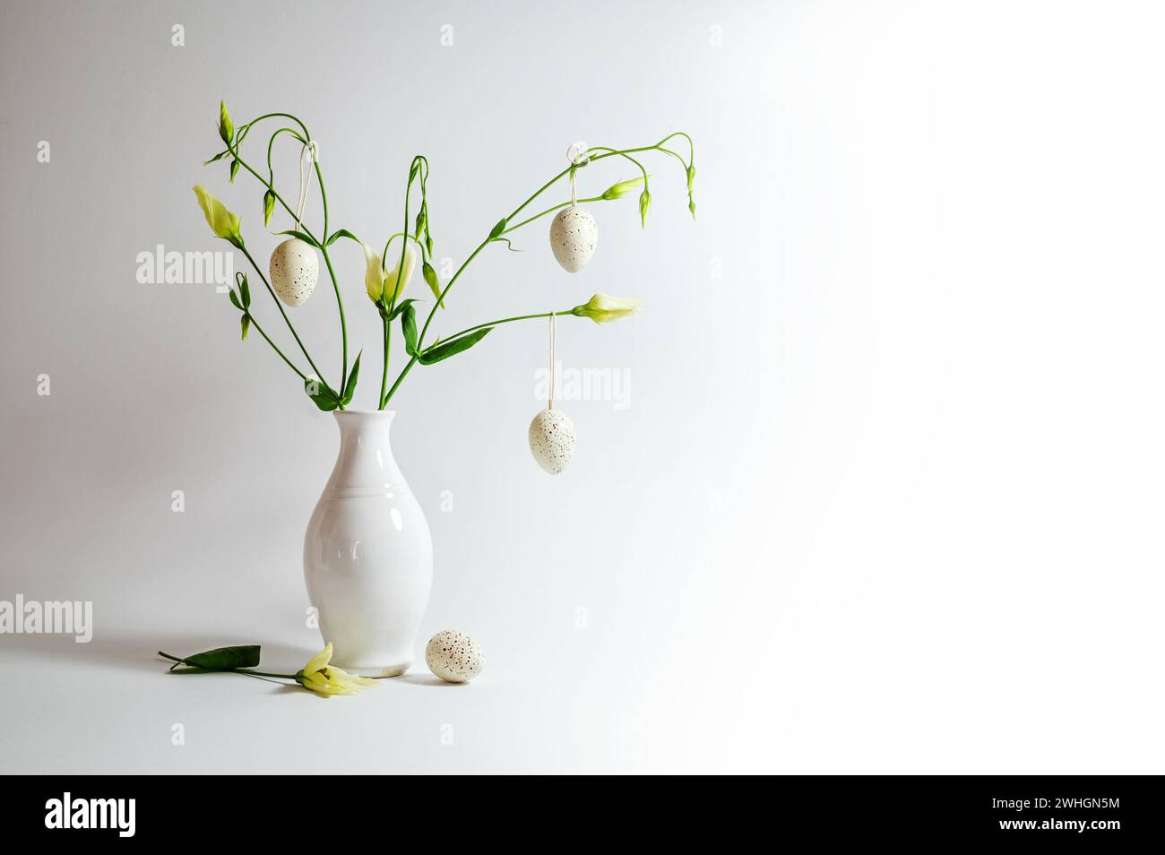 Delicate flower bunch in a white vase decorated with hanging Easter eggs on a light gray background, copy space, selected focus Stock Photo