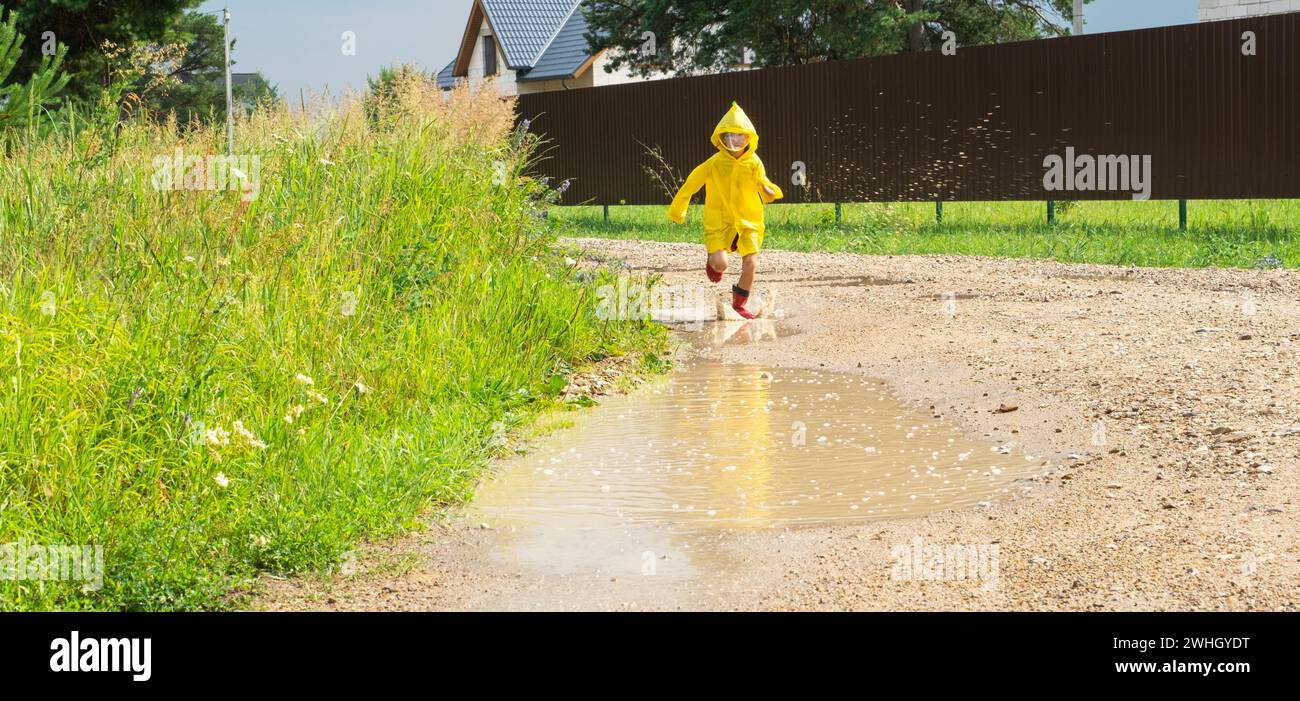 A girl in red rubber boots and a yellow raincoat runs through puddles ...