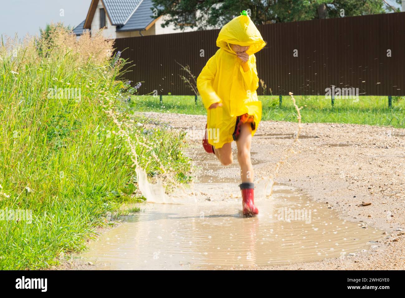 A girl in red rubber boots and a yellow raincoat runs through puddles ...