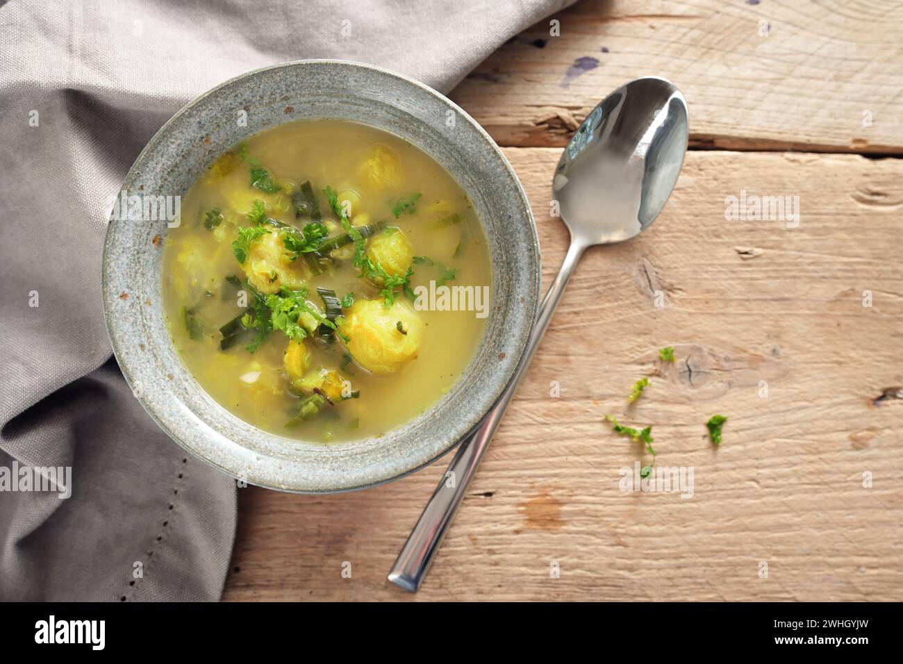 Vegetable soup with brussels sprout, leek and potato in a bowl, spoon and napkin on a rustic wooden table, high angle view from Stock Photo