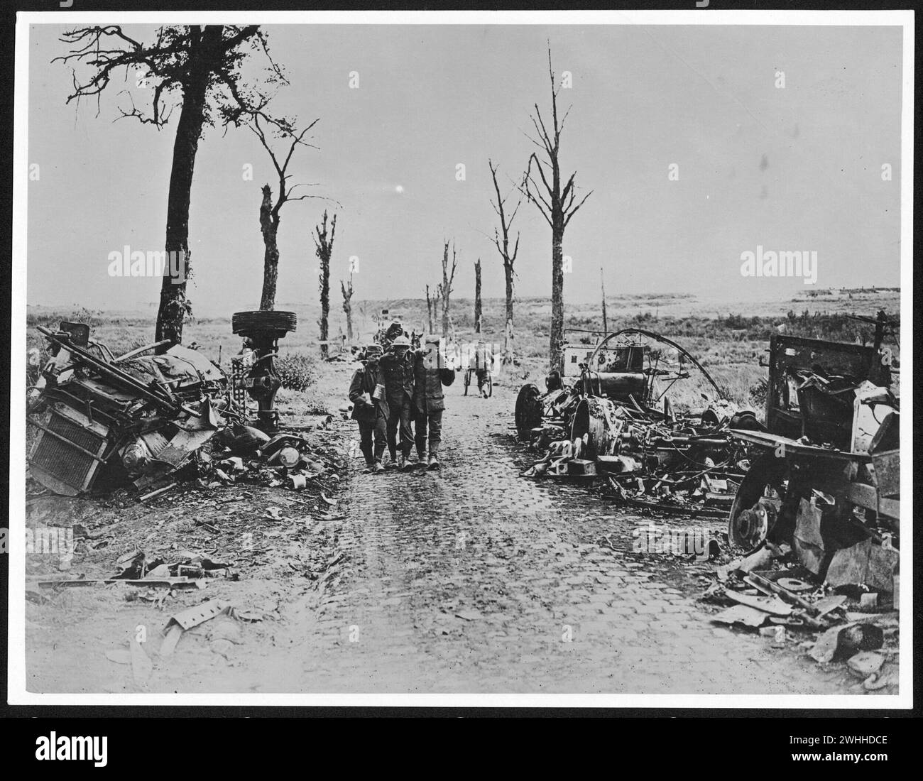 Summer 1918: German soldiers supporting an injured Canadian near Arras, in France, during World War I.  The destroyed vehicles and burnt trees framing the trio of men are, in contrast, a sharp reminder of war's destructiveness. Dates / between :26 August 1918-3 September 1918 Stock Photo