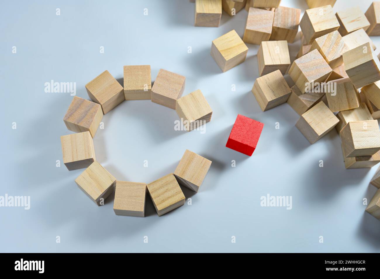 Many wooden cubes, some of them together forming a circle with a gap, one in red color is ready to complete the team, light blue Stock Photo