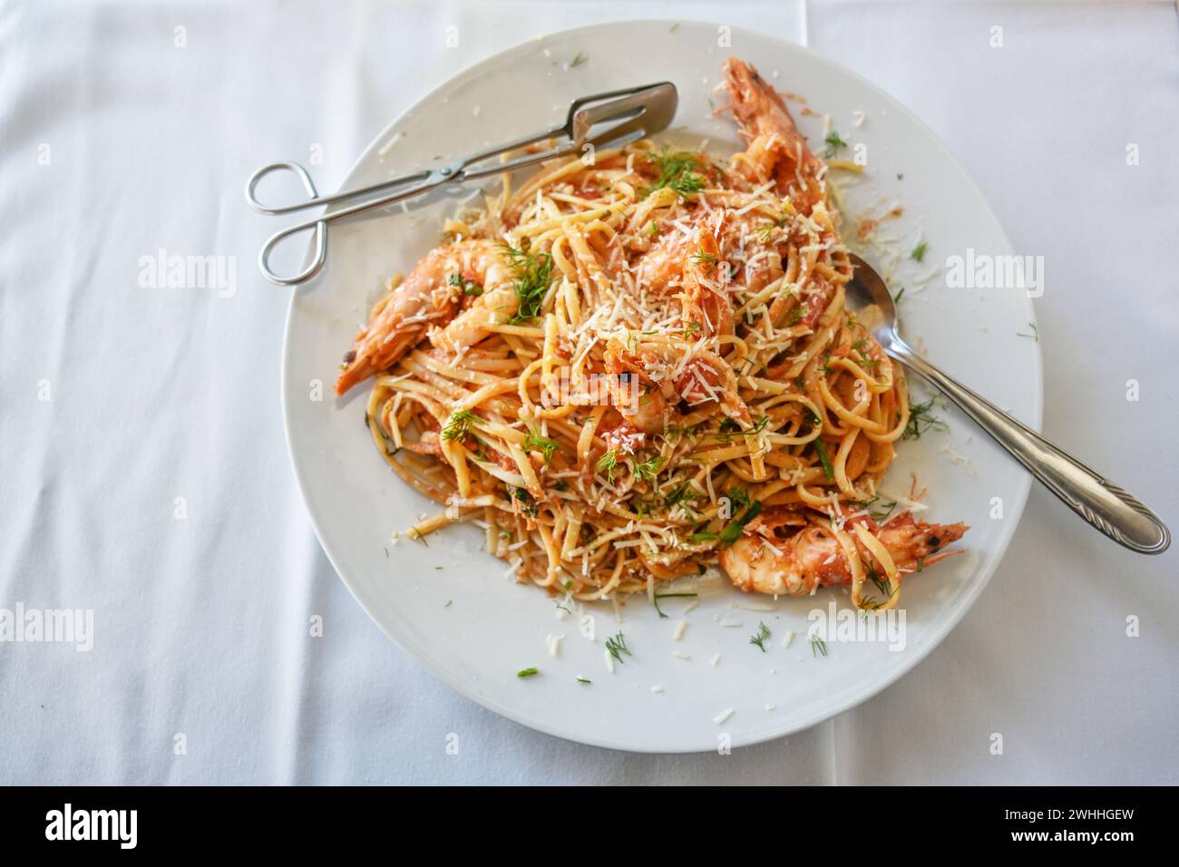 Spaghetti with shrimps in tomato sauce garnished with herbs and parmesan cheese on a plate and a white tablecloth, high angle vi Stock Photo
