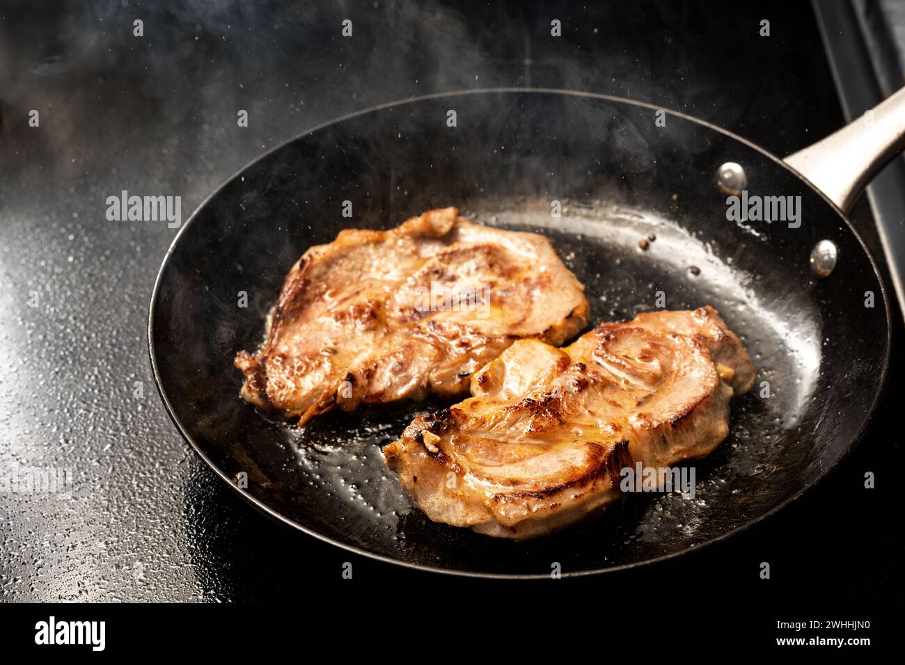 Pork steak is fried in hot splattering and steaming oil in a black iron