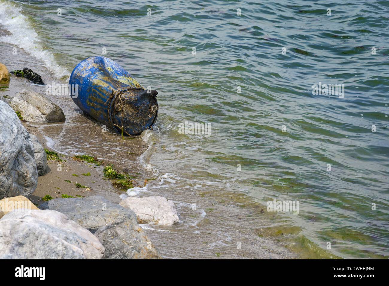 Alluvial metal barrel on the beach shore of the Mediterranean Sea in Greece, torn loose from a shellfish farm in deeper water, g Stock Photo