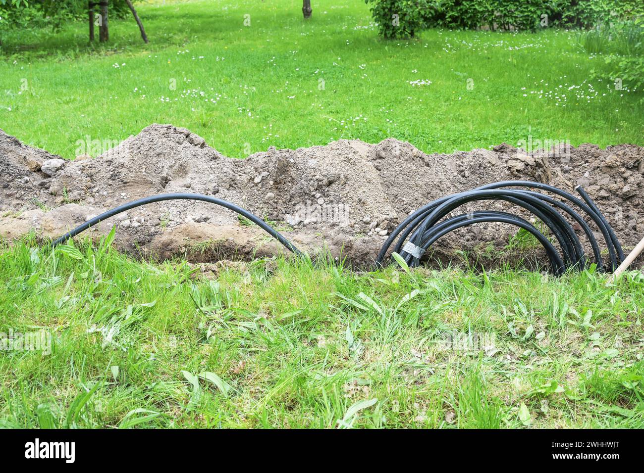 Black power cable is laid in a narrow trench in the grass across the garden, because it is a safer power supply than overhead li Stock Photo