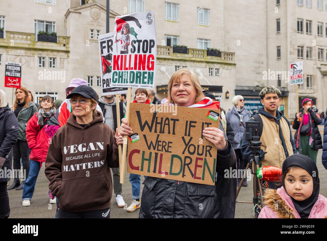 Leeds, UK. 10 FEB, 2024.  Smiling demonstrator holds 'What if it were your children' sign in city square in Leeds. Credit Milo Chandler/Alamy Live News Stock Photo
