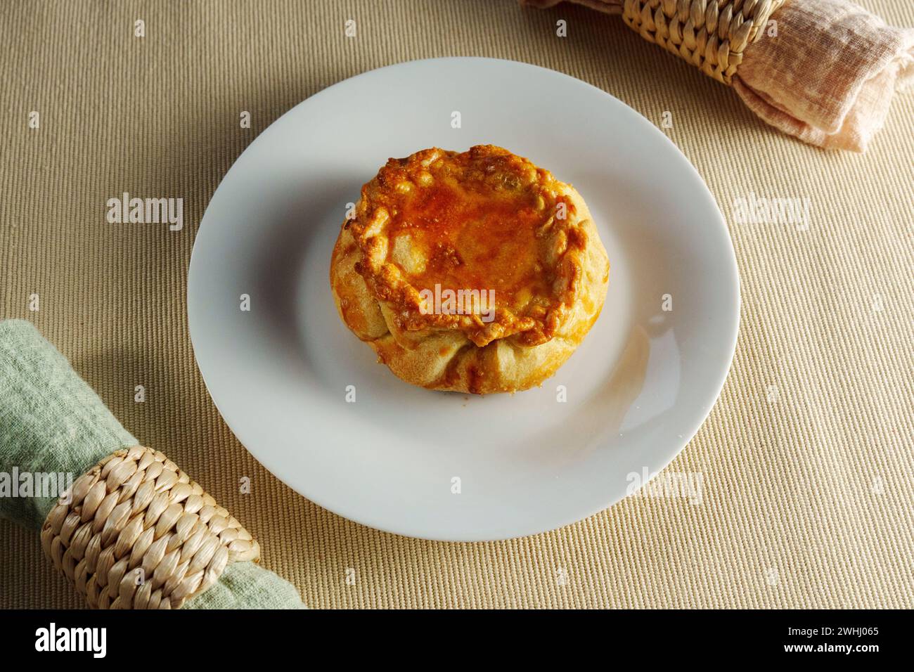 A mouthwatering pastry perches atop a pristine white plate, enticing viewers with its flaky layers and irresistible aroma. Stock Photo