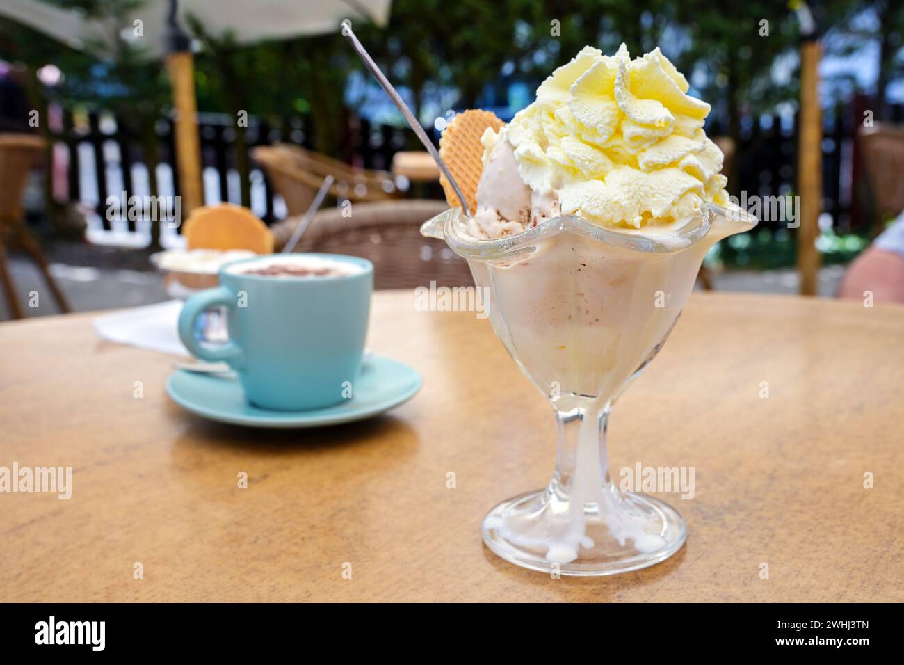 Ice cream sundae in a glass bowl and a coffee cup on the table in an outdoor cafe, delicious sweet dessert and refreshment in su Stock Photo