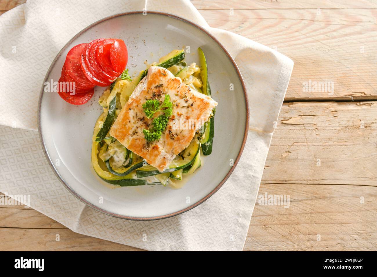 Wild salmon fillet with parsley garnish, zucchini vegetables and tomato on a light plate and a rustic wooden table, healthy low Stock Photo