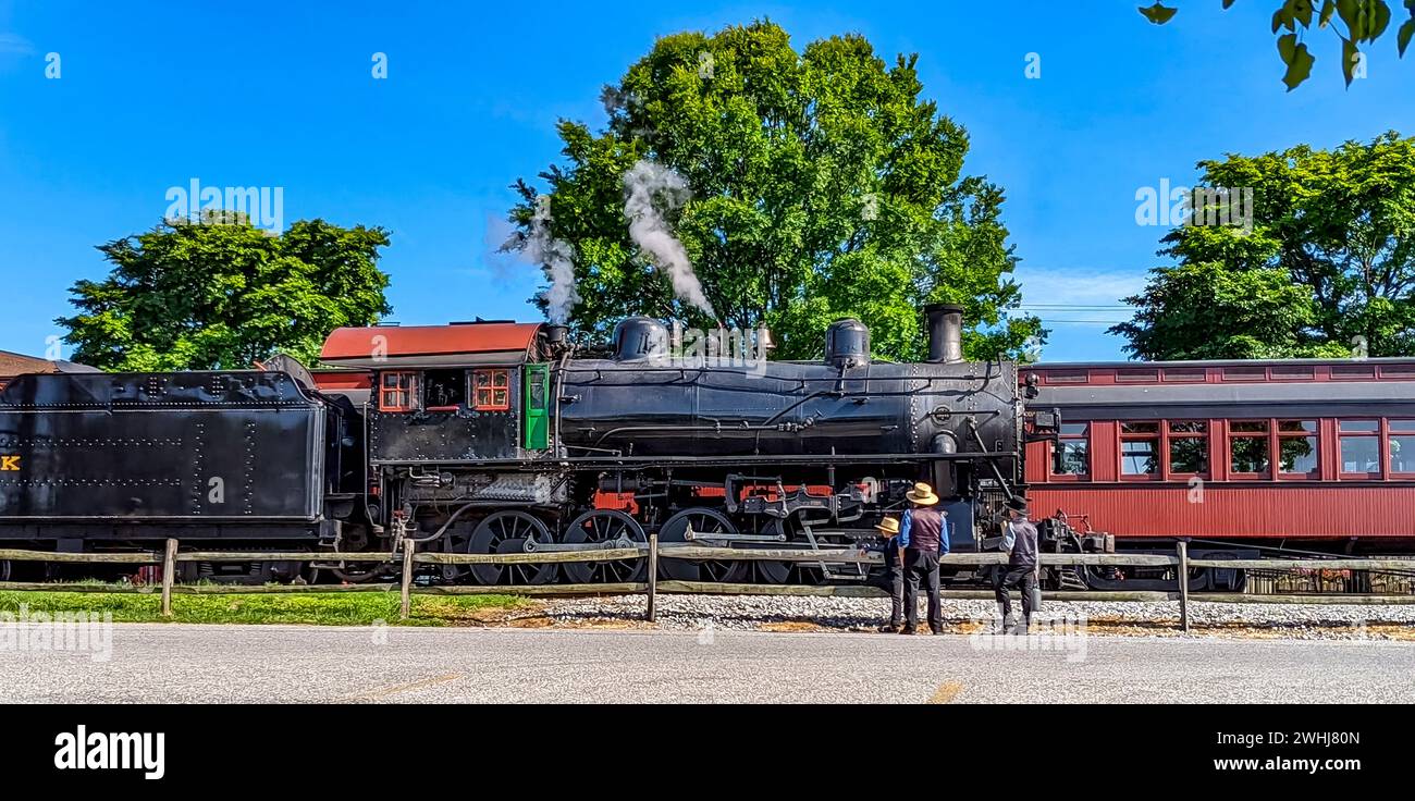 View of an Amish Father and His Sons Looking at an Old Steam Engine Warming Up Blowing Steam Stock Photo