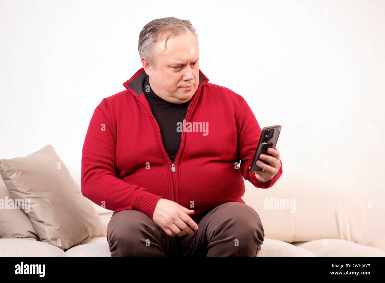 man talking or watching something on his phone while sitting on the sofa Stock Photo