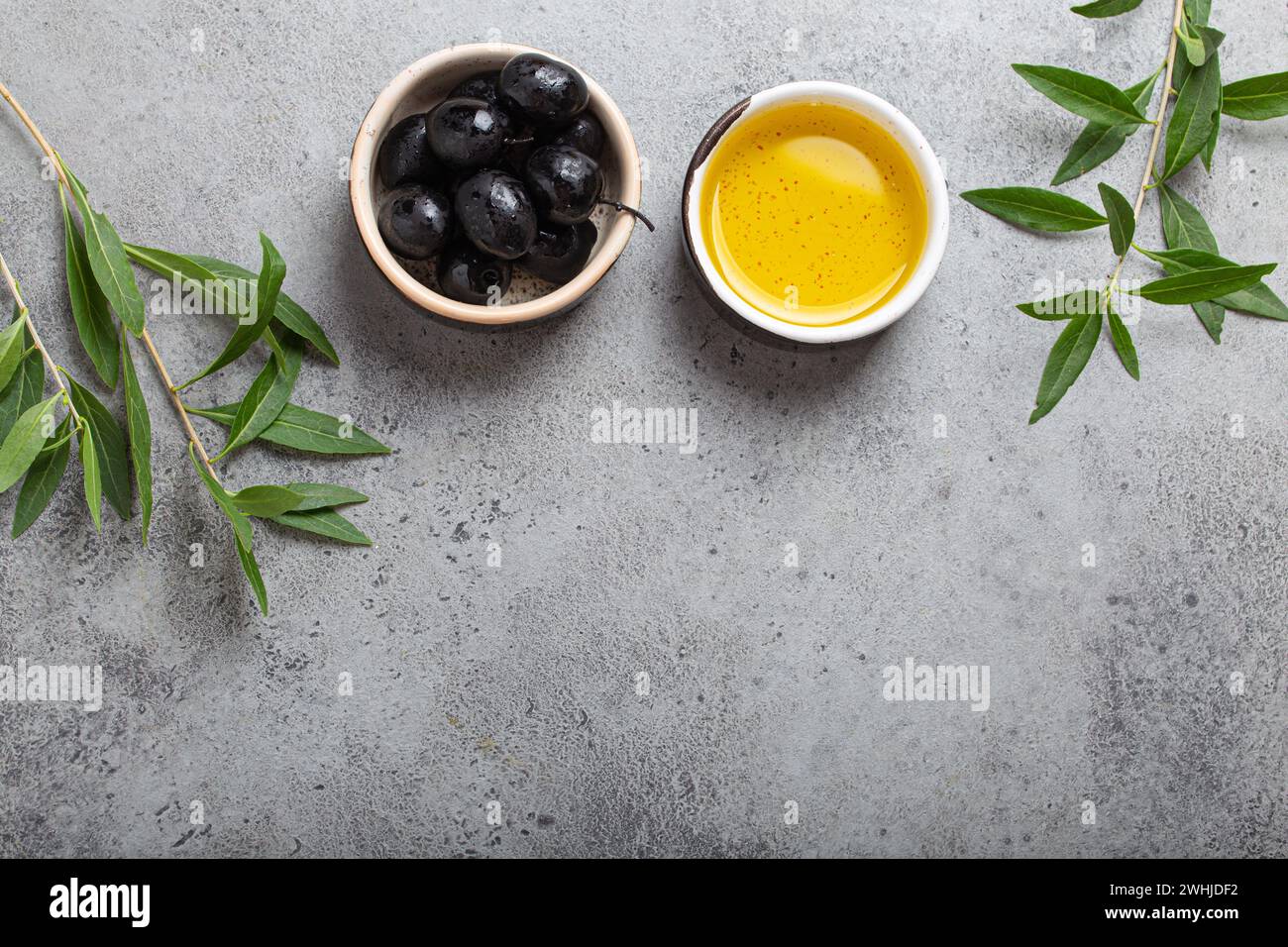 Black olives and extra virgin olive oil in little bowl with olive tree branches top view on grey concrete stone background, spac Stock Photo