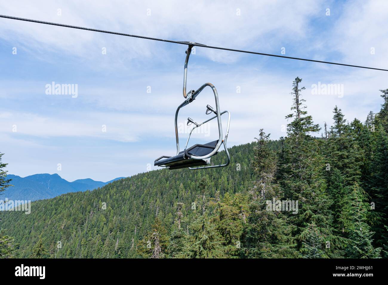 An empty chairlift chair elevated above a forest with lush mountains in ...