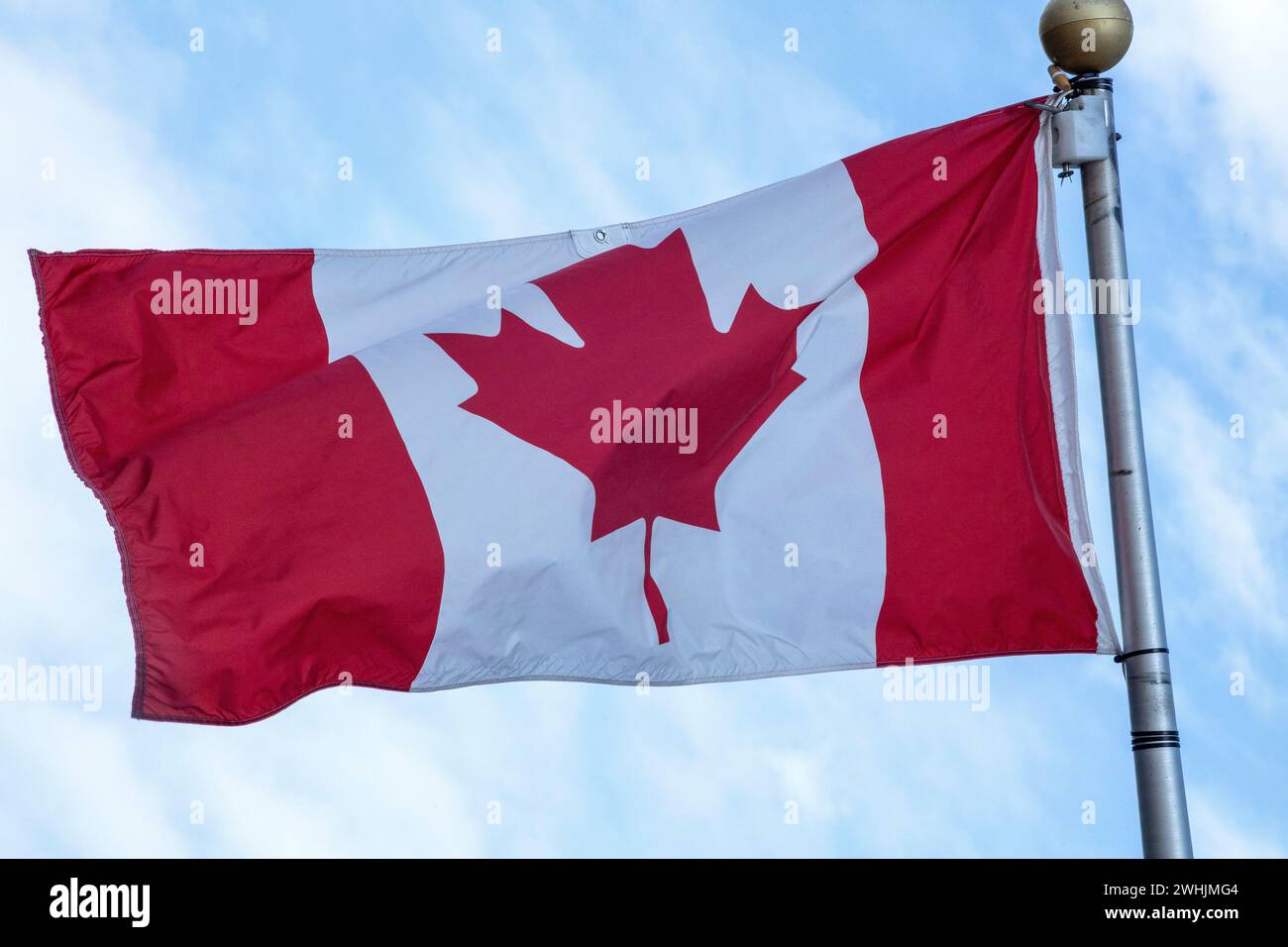 Canadian Flag flying in the wind outdoors on a sunny summers. Blue sky background with clouds. Stock Photo