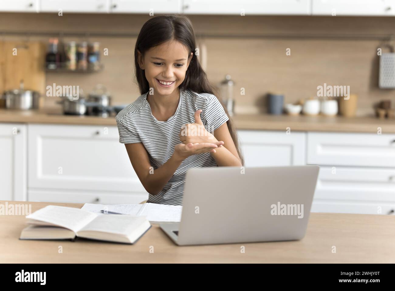 Positive pre teen schoolkid girl with hearing disability using laptop Stock Photo
