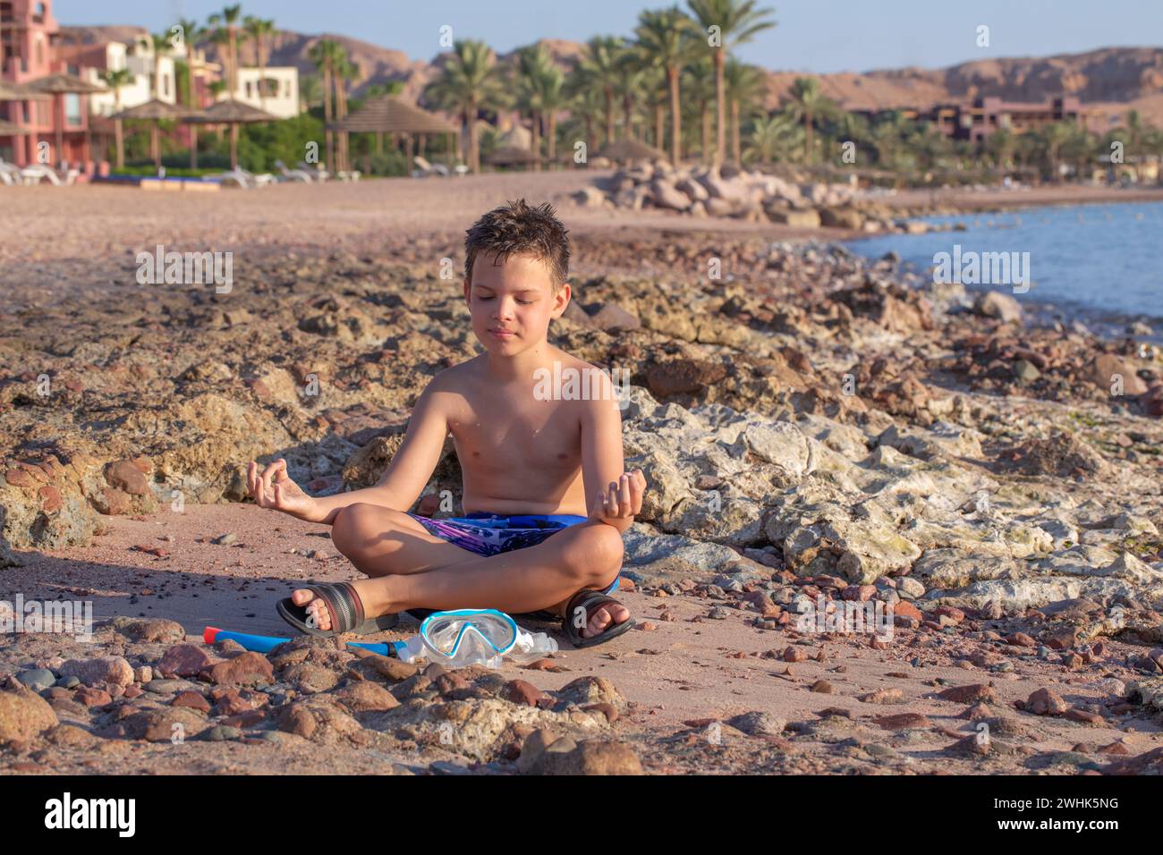 A little boy of 9 years old is sitting at the beach of the seaside along the Red Sea, Tala Bay, Aqaba, Jordan Stock Photo