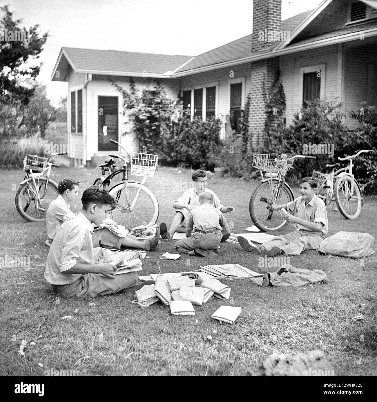 Group of boys folding newspapers on front yard lawn before delivering them in the afternoon, Natchitoches, Louisiana, USA, Marion Post Wolcott, U.S. Farm Security Administration, June 1940 Stock Photo