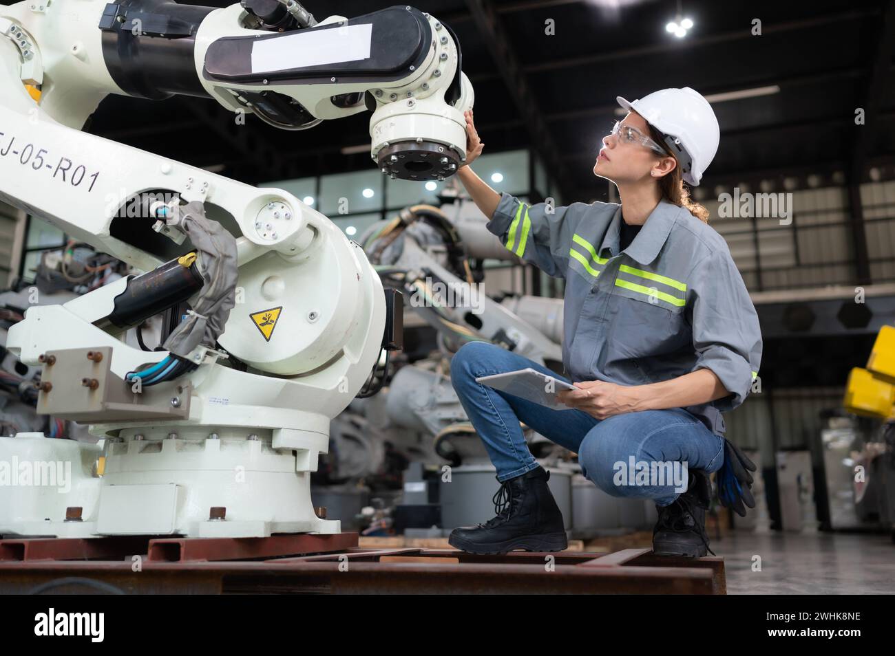 A female engineer installs a program on a robotics arm in a robot warehouse. And test the operation before sending the machine t Stock Photo