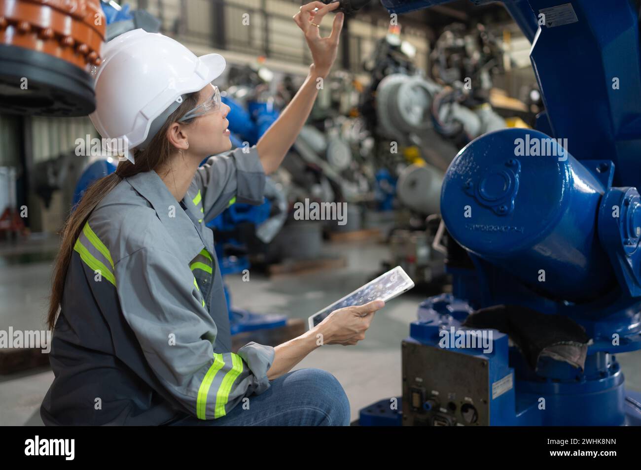 A female engineer installs a program on a robotics arm in a robot warehouse. And test the operation before sending the machine t Stock Photo