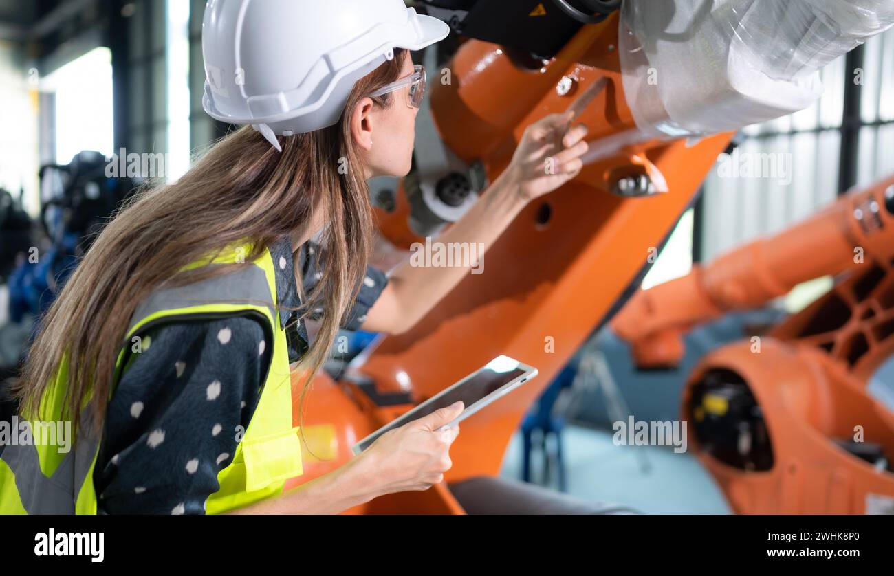 A female engineer installs a program on a robotics arm in a robot warehouse. And test the operation before sending the machine t Stock Photo